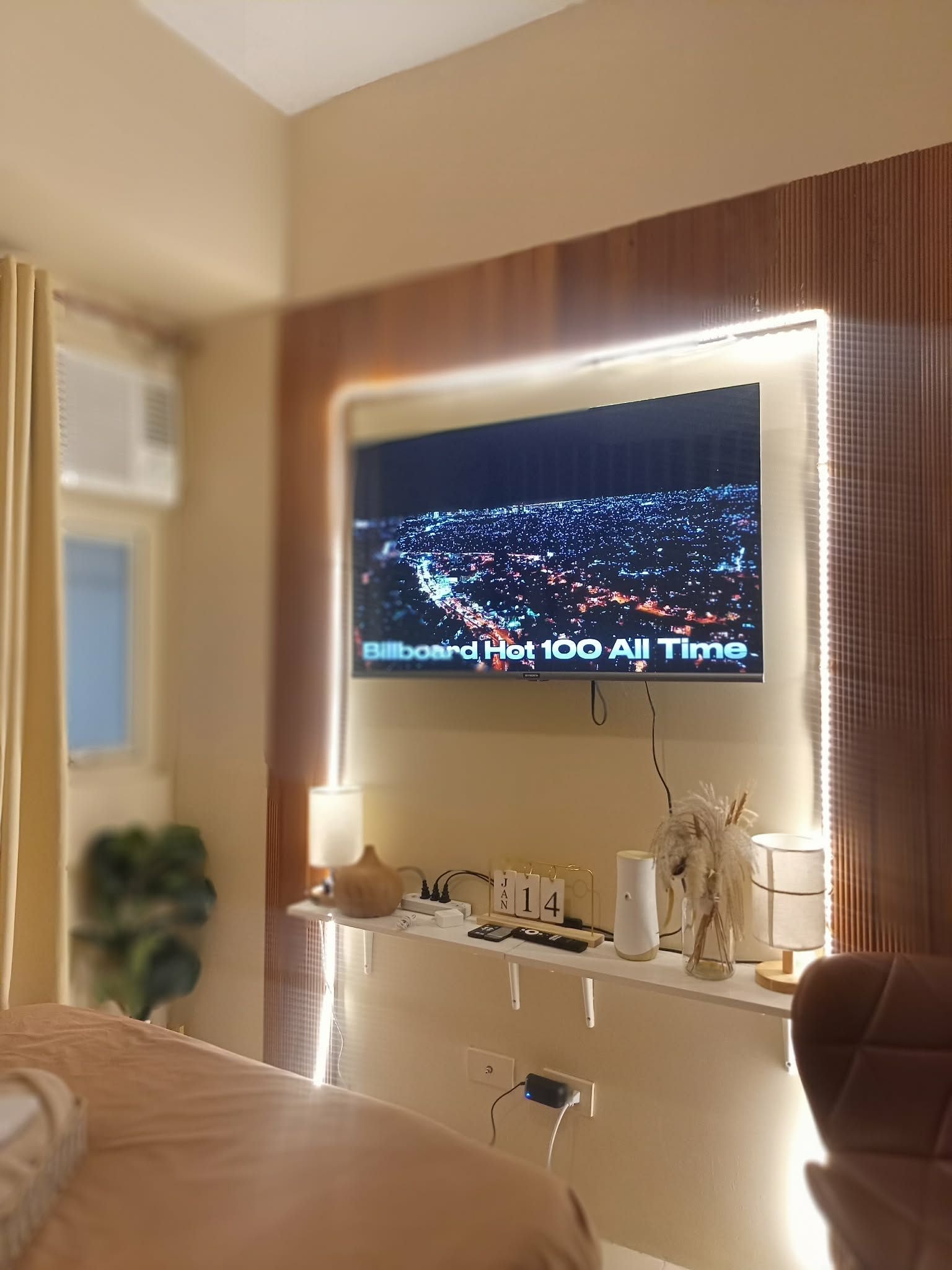 A hotel room with a large flat-screen TV mounted on the wall displaying a cityscape.