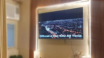 A hotel room with a large flat-screen TV mounted on the wall displaying a cityscape.