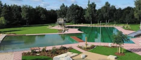 A swimming pool with a diving platform, surrounded by a grassy area and trees.