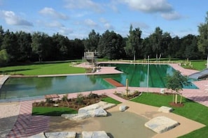 En swimmingpool med en hoppställning, omgiven av en gräsyta och träd.