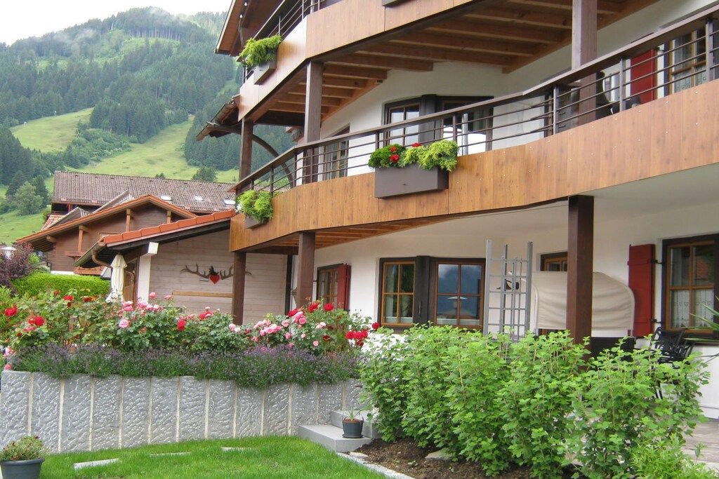A multi-story building with balconies, a stone wall, and a garden with flowers.