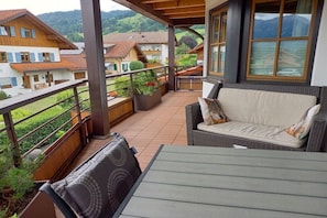 A balcony with a sofa and table, overlooking a residential area with houses and a mountain. - Eldorado Holiday Apartment Southwind (Bolsterlang)