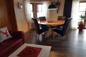 A cozy living room with a red sofa, a white table with a red placemat, and a dining area with a round table and chairs. - Eldorado Holiday Apartment Southwind (Bolsterlang)