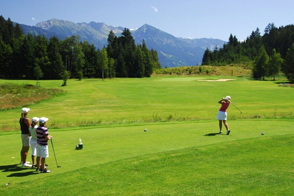 A golf course with a mountainous backdrop, a putting green, and players in action.
