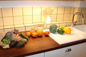 Eine Küchenarbeitsplatte mit verschiedenen Früchten und Gemüsesorten, einer Karaffe und einem Spülbecken.