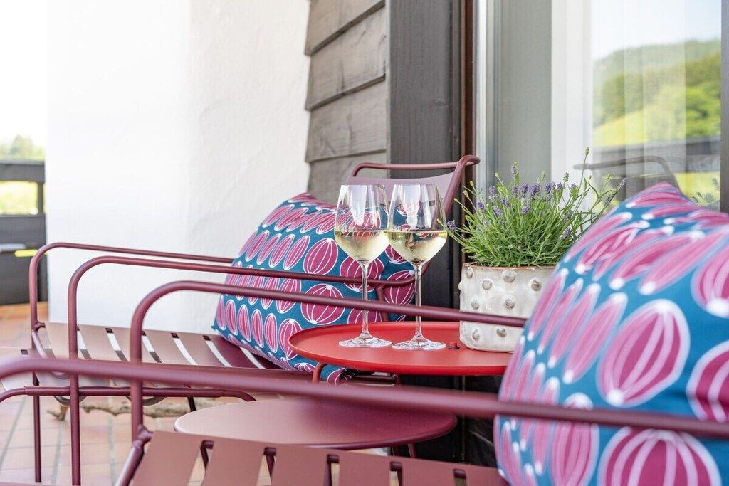 Eine Terrasse mit Metallstühlen und einem Tisch, zwei Gläsern Weißwein und einem Blumentopf.