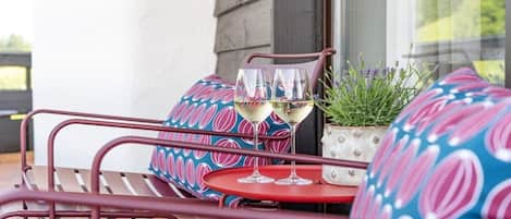 A patio with metal chairs and a table, two glasses of white wine, and a potted plant.
