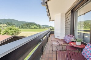 Ein Balkon mit Blick auf eine grüne Landschaft, ein Tisch mit einer Pflanze und zwei Stühle.