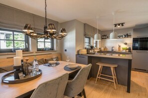 Eine moderne Küche mit einer zentralen Kochinsel, Pendelleuchten und einem Essbereich mit Holztisch und Stühlen.