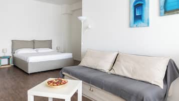 A modern bedroom with a bed, a sofa, a small table with a bowl of fruit, and a floor lamp.