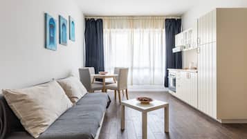 A compact living space with a sofa, a dining table with chairs, a small kitchen area, and a window with curtains.