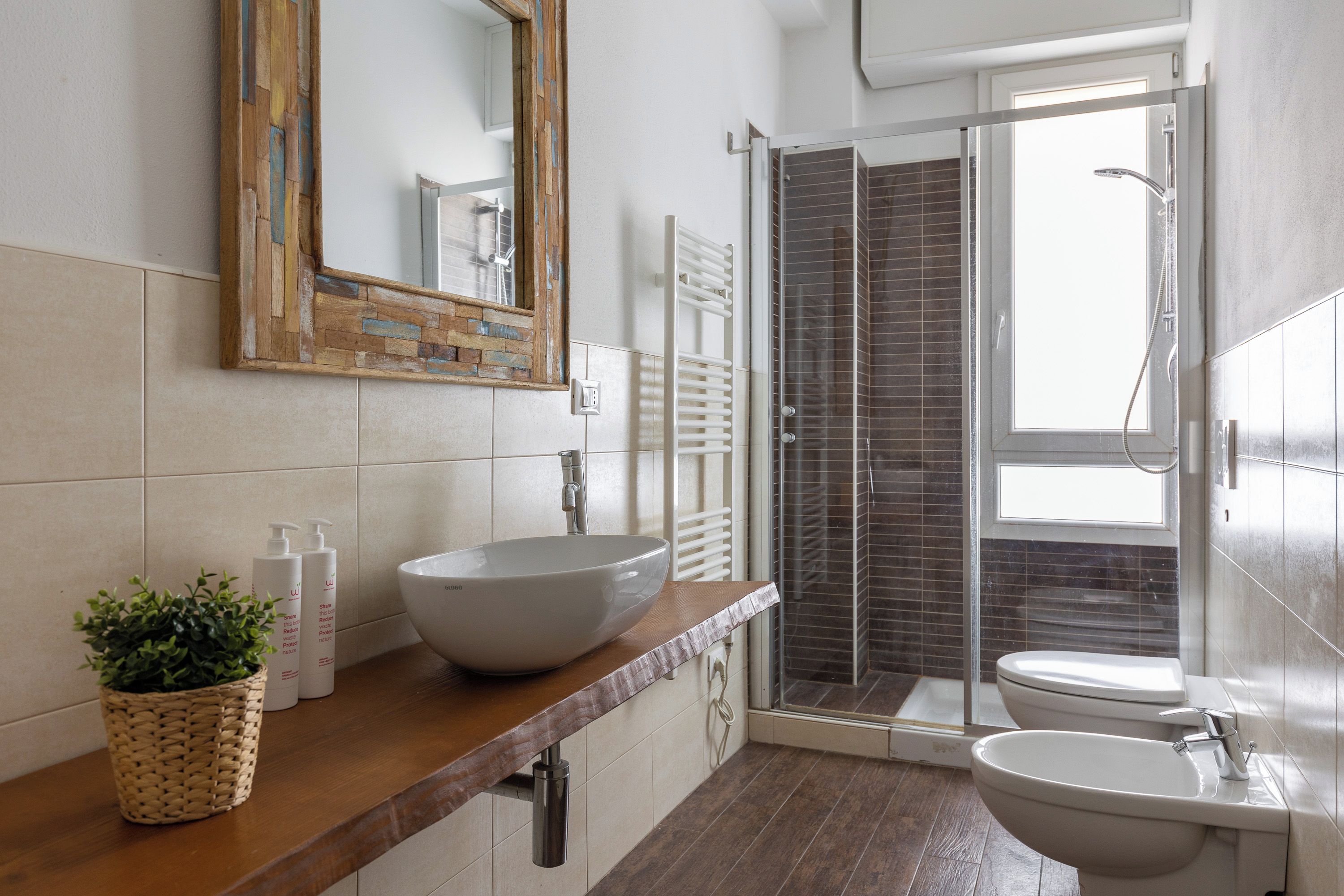 A modern bathroom with a large mirror, a vessel sink, a bidet, and a shower area.