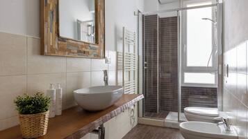 A modern bathroom with a large mirror, a vessel sink, a bidet, and a shower area.