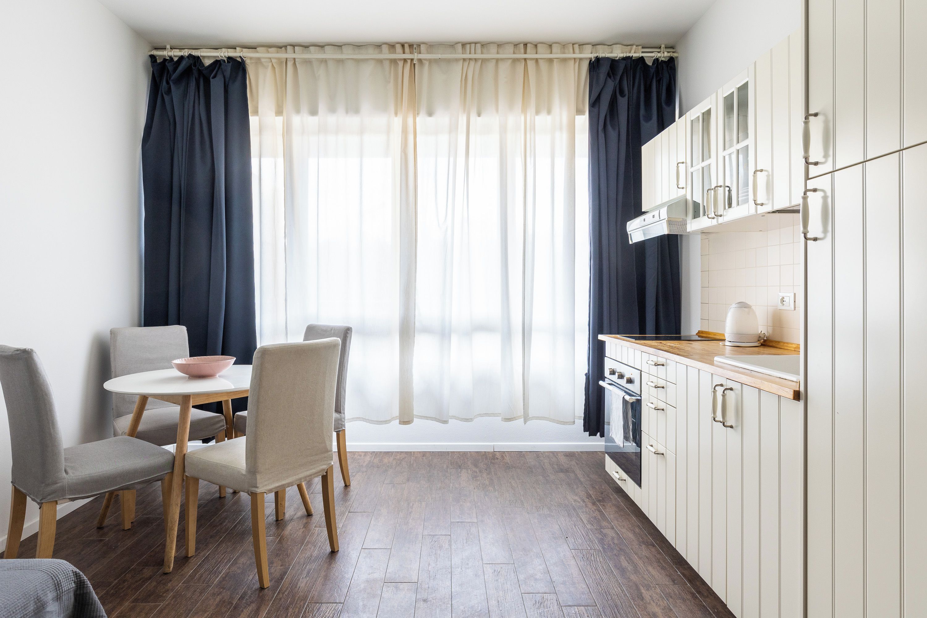 A compact kitchen with a dining area, featuring a table with chairs, a stove, and cabinets.