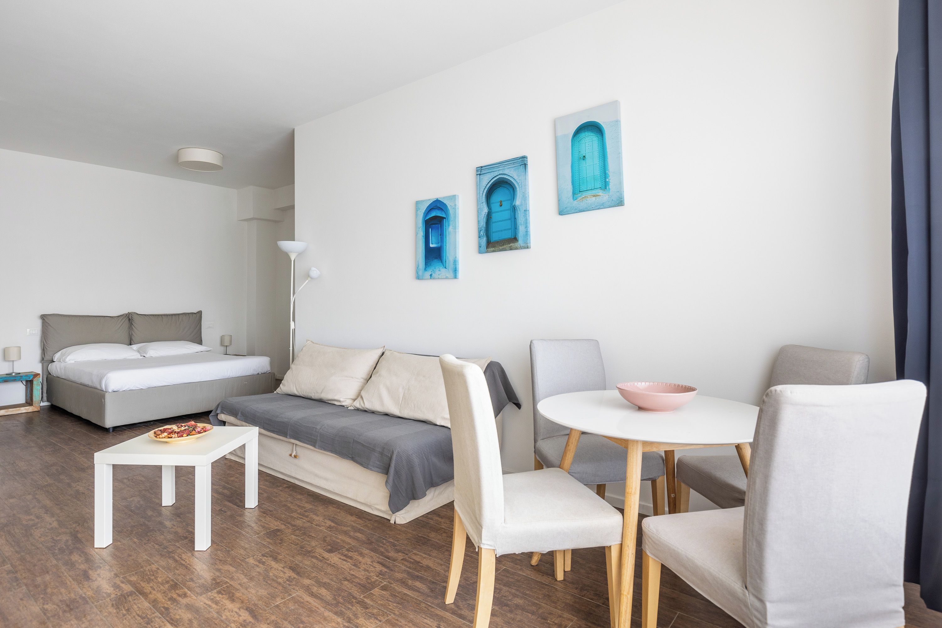 A modern, well-lit hotel room with a bed, sofa, dining table, and chairs.