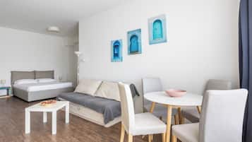 A modern, well-lit hotel room with a bed, sofa, dining table, and chairs.