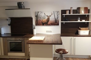 Eine moderne Küche mit Einbauofen, Holz Arbeitsplatte, Barhocker und einer Wandablage mit Küchenutensilien.