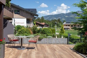 Une terrasse avec deux chaises et une table, un bâtiment avec une enseigne et une vue sur la montagne.
