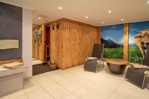 Ein Zimmer mit Holzwand, Massage-Sessel, Massagetisch und einer großen Wandmalerei von einer Kuh und Bergen.