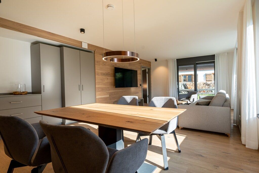 A modern dining area with a wooden table and chairs, a sofa, and a television mounted on the wall.