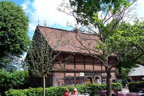 Ein traditionelles Gebäude mit Ziegeldach und Backsteinwänden, umgeben von viel Grün.