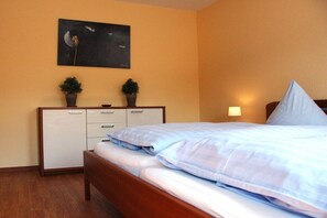 Une chambre d’hôtel avec un lit, un bureau doté de tiroirs, une petite plante en pot et un tableau accroché au mur.