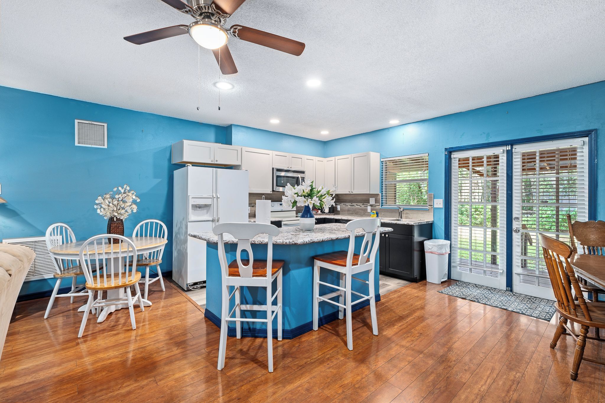 A modern kitchen with white cabinets, a central island with bar stools, and a ceiling fan.