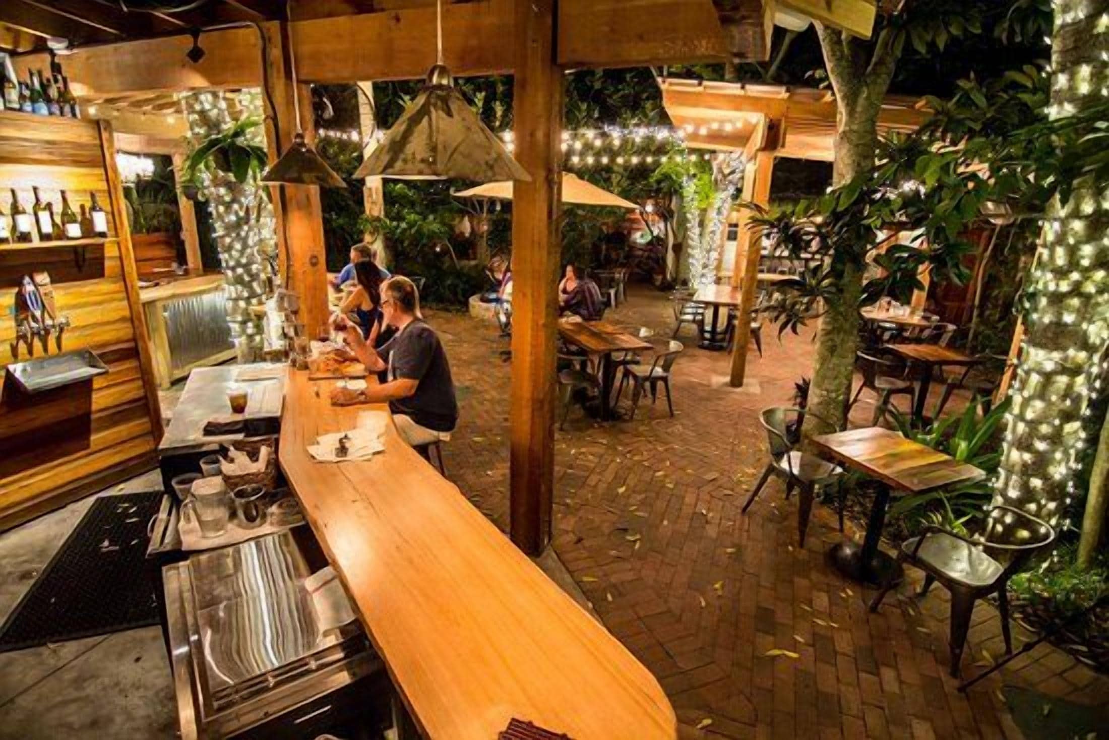 An outdoor dining area with tables and chairs, a bar counter, and hanging lights.