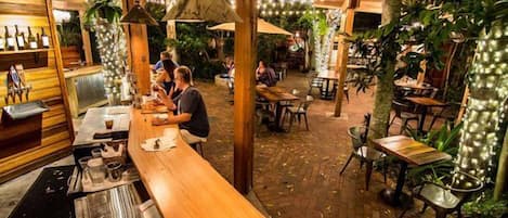 An outdoor dining area with tables and chairs, a bar counter, and hanging lights.