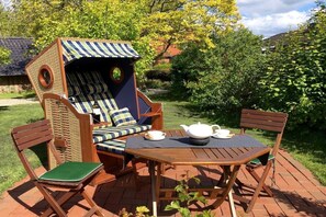 Eine Holzterrasse mit einem Sitzbereich im Streifenmuster, einem Tisch mit Teekanne und Tasse.