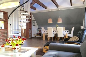 Ein modernes Wohnzimmer mit Treppe, Essbereich und einer Sitzecke inklusive Sofa und Sessel.