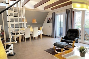 Ein modernes Wohnzimmer mit Treppe, Essbereich und schwarzem Ledersessel.