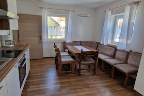 A compact kitchen with a dining area, wooden furniture, and a window with curtains. - Holiday apartment with 2 bedrooms (Pottenstein)
