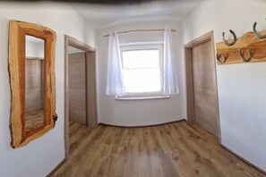 A room with a wooden floor, a window with white curtains, a wooden door, and a wall-mounted coat rack. - Holiday apartment with 2 bedrooms (Pottenstein)