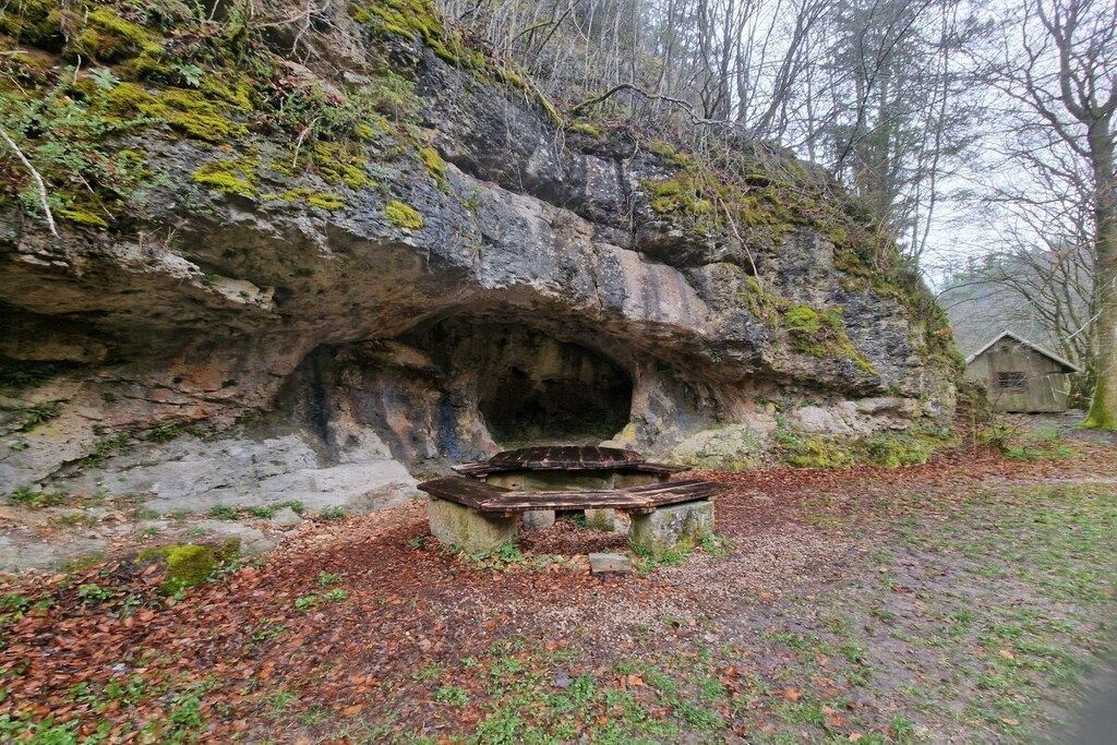 Une structure en forme de grotte, avec un banc devant.