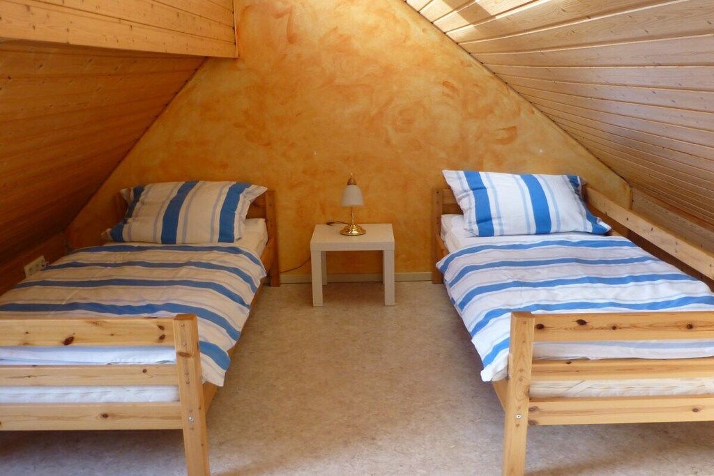 A small attic bedroom with two wooden beds, a nightstand, and a lamp.