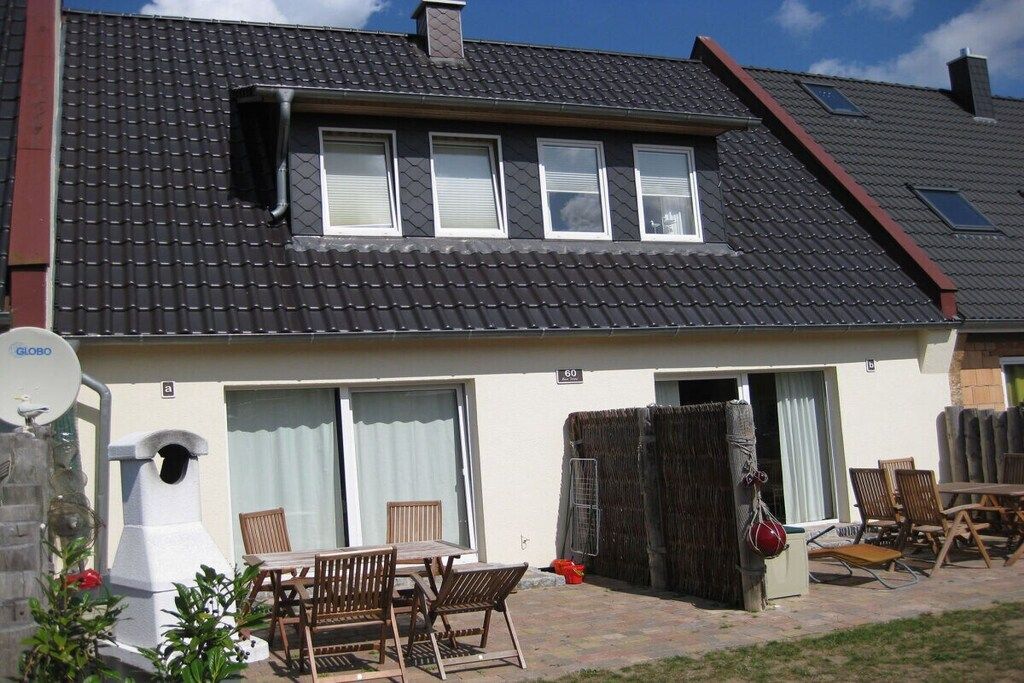Ein Wohngebäude mit einem Ziegeldach, einer Satellitenschüssel, einer überdachten Terrasse mit Gartenmöbeln und der Hausnummer 60 an der Wand.