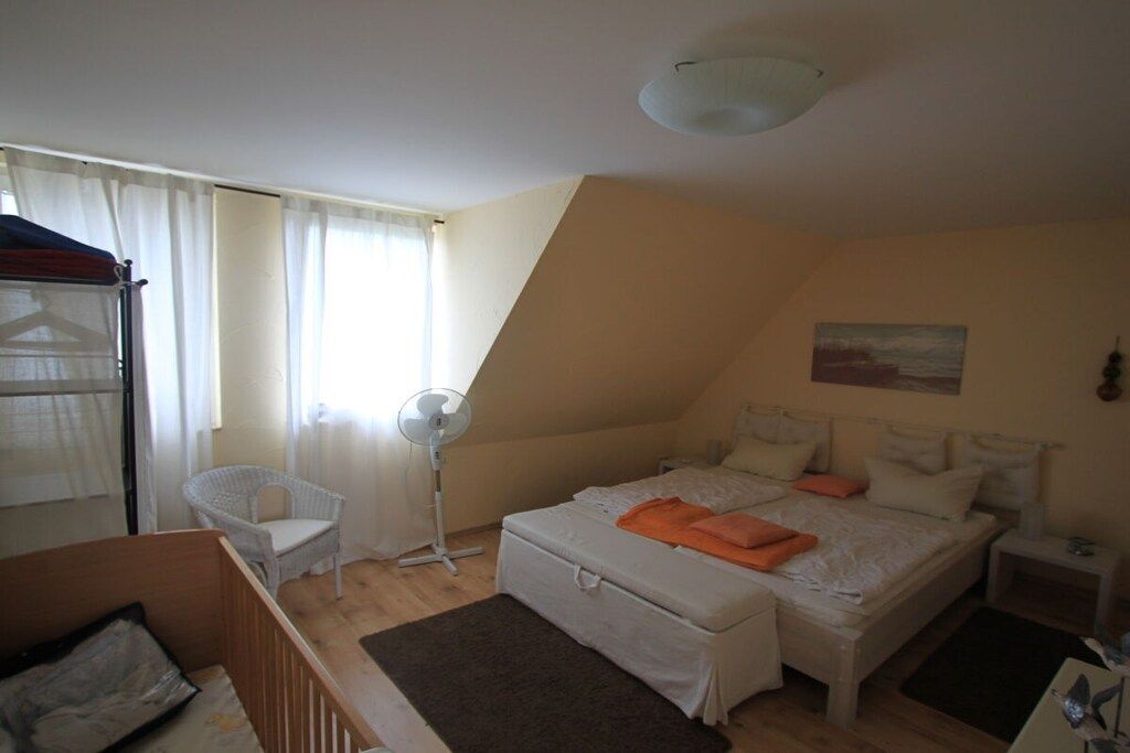 A bedroom with a bed, a chair, a bedside table, and a window with curtains.