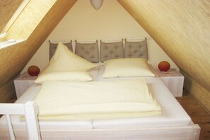 Una cama individual con cabecera, dos mesitas de noche y un objeto redondo pequeño sobre la mesa de la izquierda.