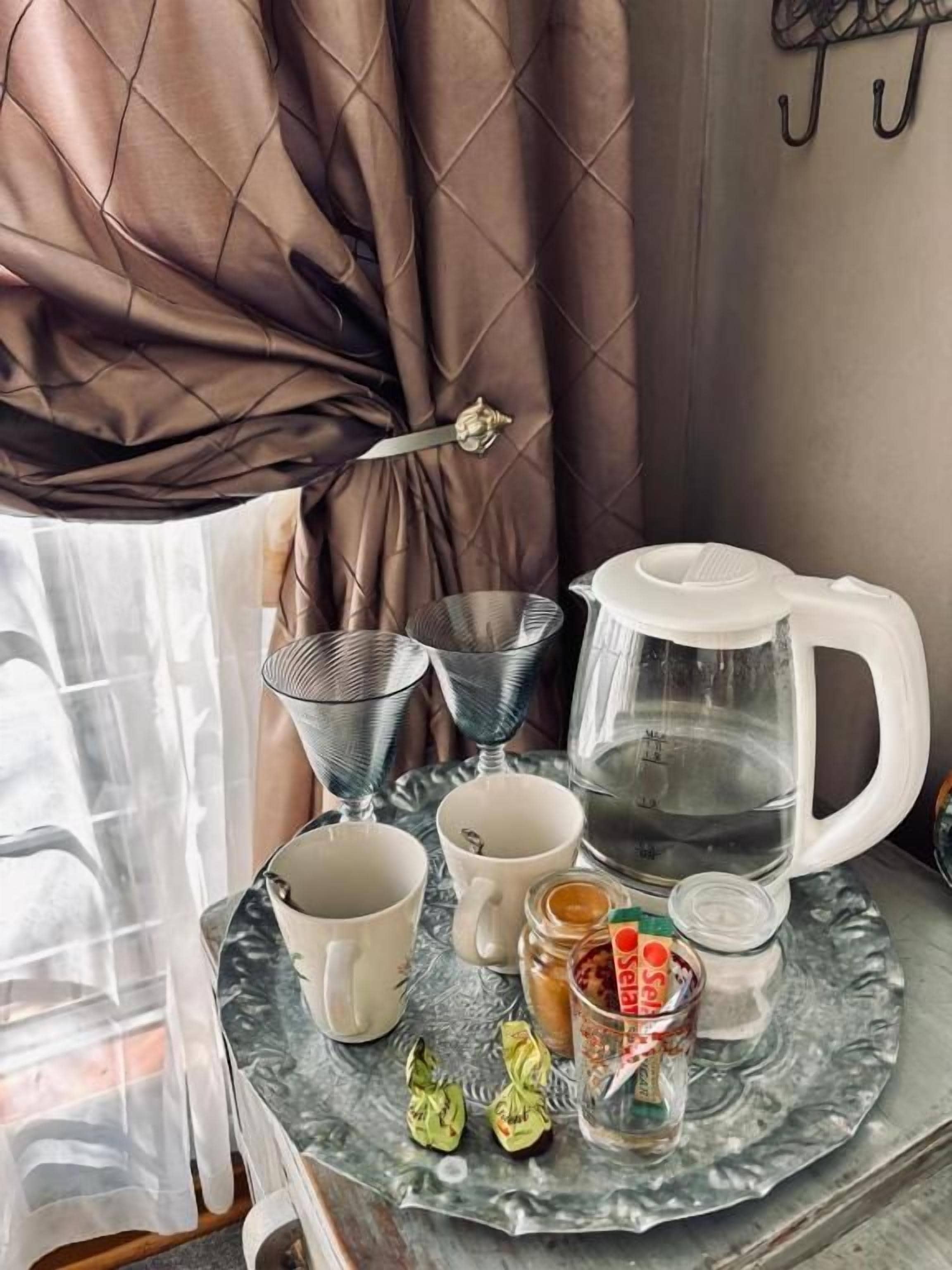 A tray with a coffee maker, two cups, a glass of water, and a jar of jam.