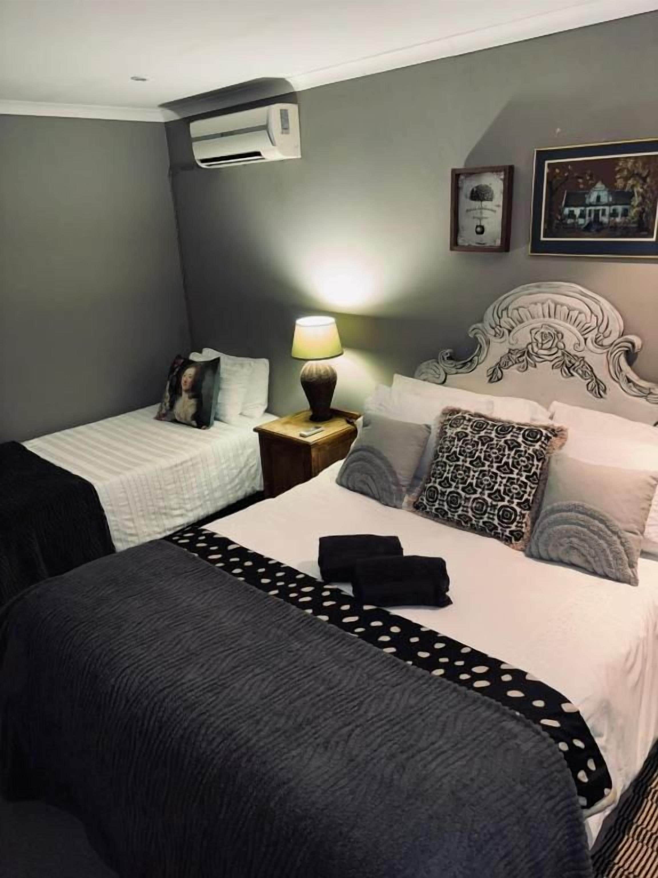 A hotel room with two beds, a nightstand with a lamp, a wall-mounted air conditioner, and framed pictures.