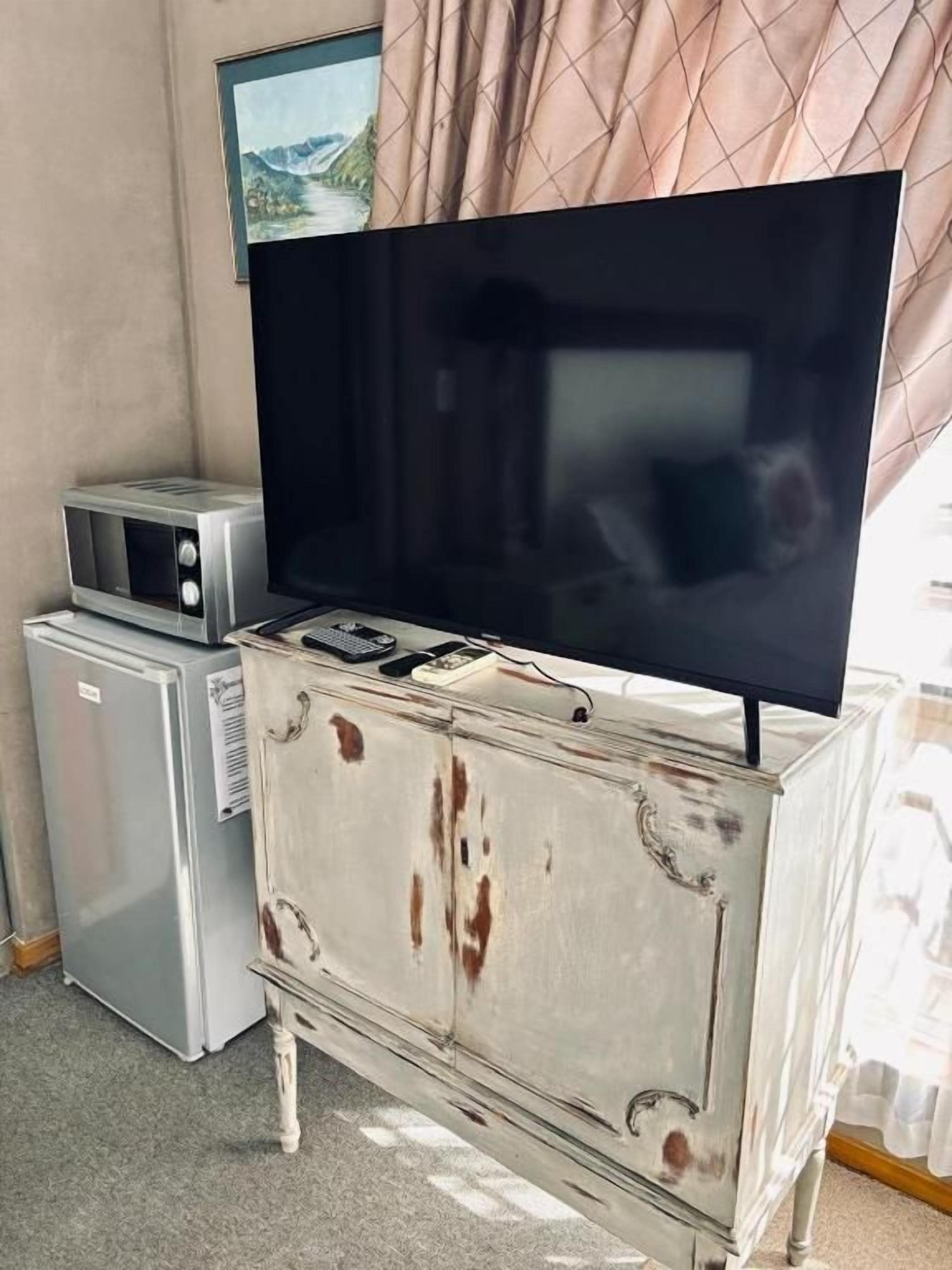 A television on a white dresser with visible wear, a microwave, and a small refrigerator.