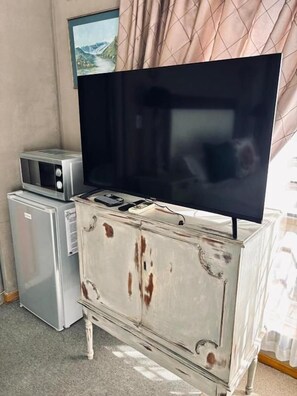 A television on a white dresser with visible wear, a microwave, and a small refrigerator. - LaGrace Guesthouse (Kroonstad)