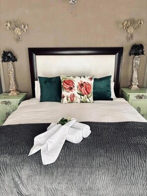 Una cama con cabecera oscura, almohadas verdes y una manta gris junto con toallas.