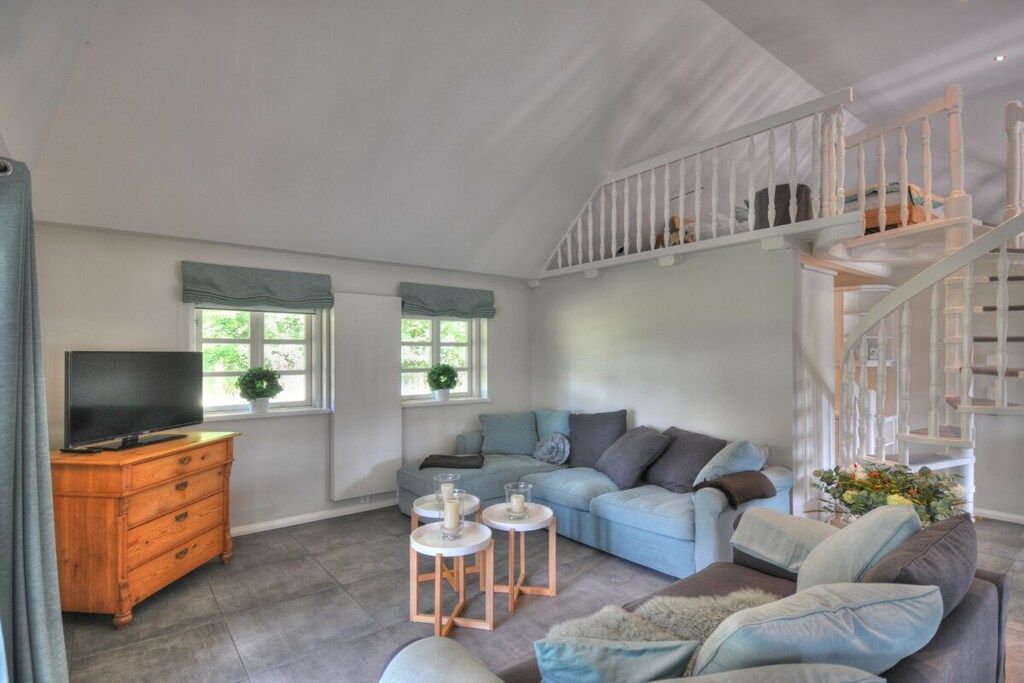 Un salon spacieux comprenant un canapé, un téléviseur, une commode en bois et un escalier.