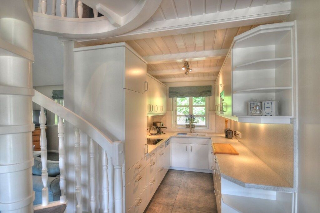 A kitchen with white cabinetry, a wooden staircase, and a window with a view of greenery.