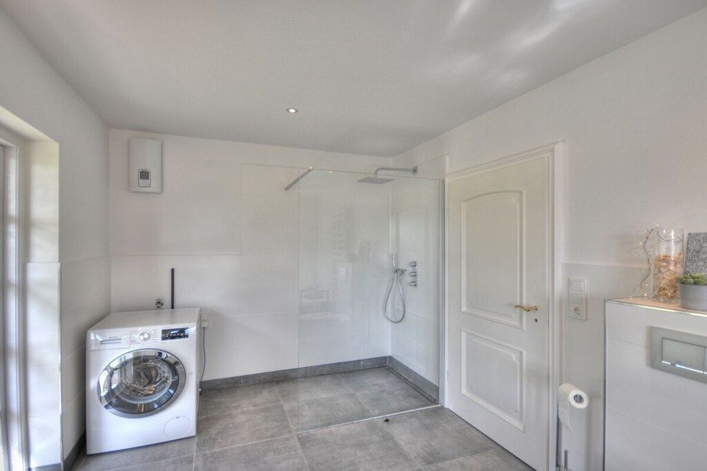 A compact bathroom with a washing machine, a glass shower enclosure, and a white door.