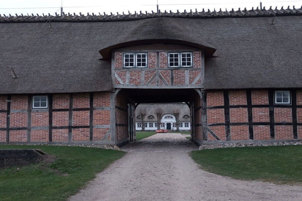 A traditional building with a thatched roof, a central archway, and a symmetrical facade with brickwork and timber framing.