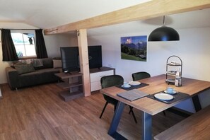 Een knus woongedeelte met een bank, een eettafel, een televisie en een boekenkast.