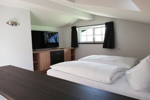 Un dormitorio con una cama, televisión, escritorio y ventana con cortinas.